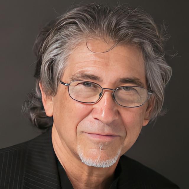 Michael Andreas poses for a headshot in front of a dark gray background.