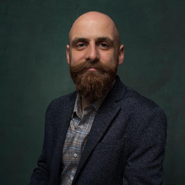 A man poses for a photo in front of a neutral background.