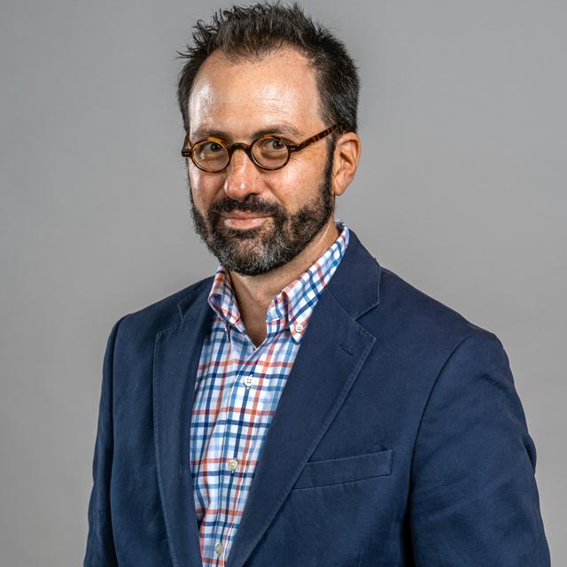 Paul Miller poses for a headshot in front of a gray background.