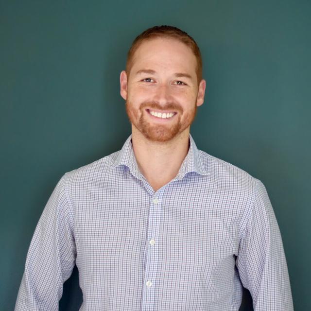 Philip Mauskapf poses for a headshot in front of a dark green background.