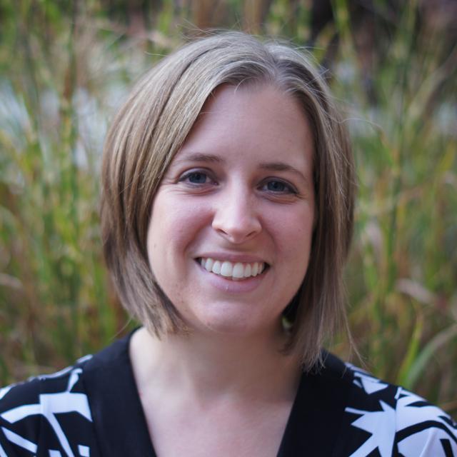 Rachel Skilone poses for a headshot outdoors in front of tall grasses.