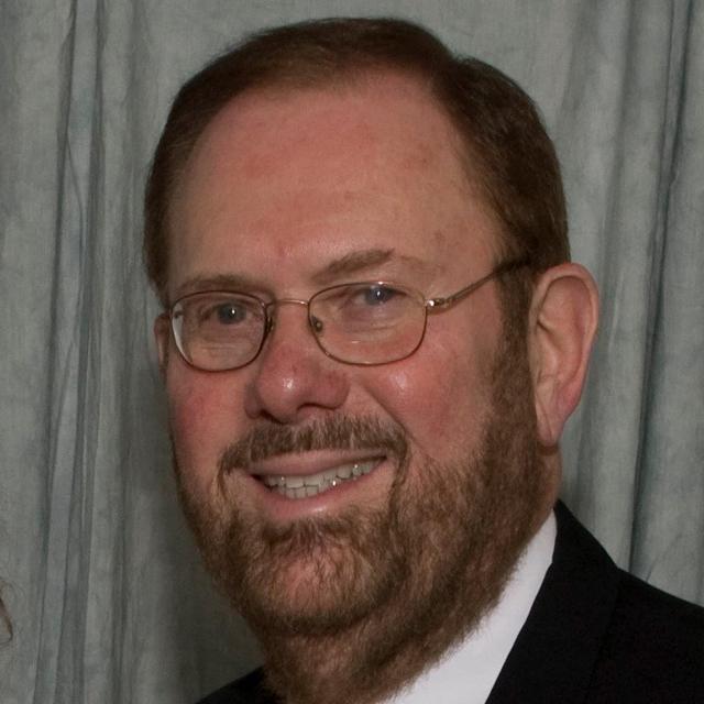 Ronald Bickel poses for a headshot in front of a gray curtain.