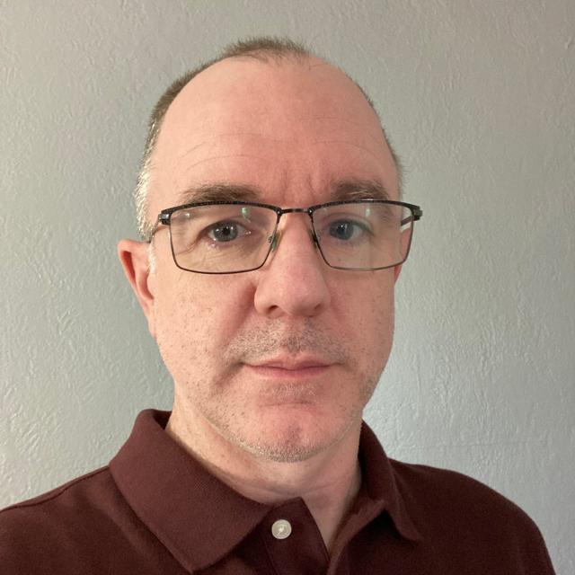 person with glasses in front of white wall