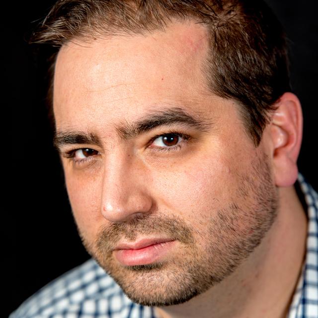 A person poses for a headshot in front of a black background.