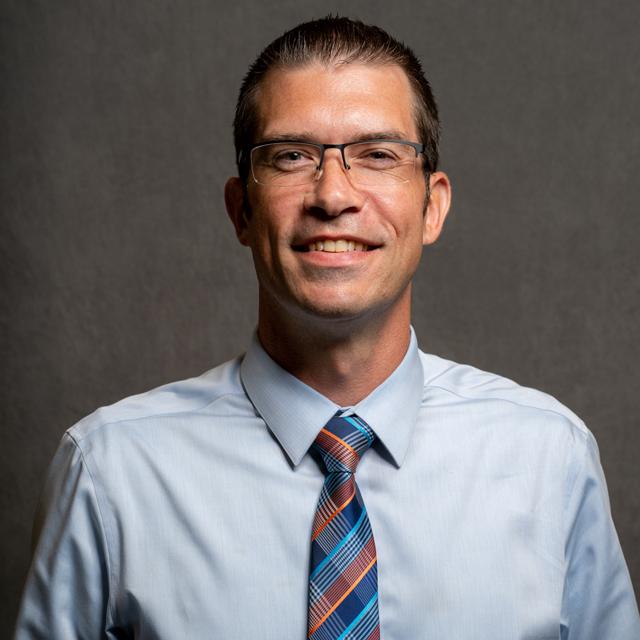 Thomas Carsecka poses for a head shot in front of a gray background.