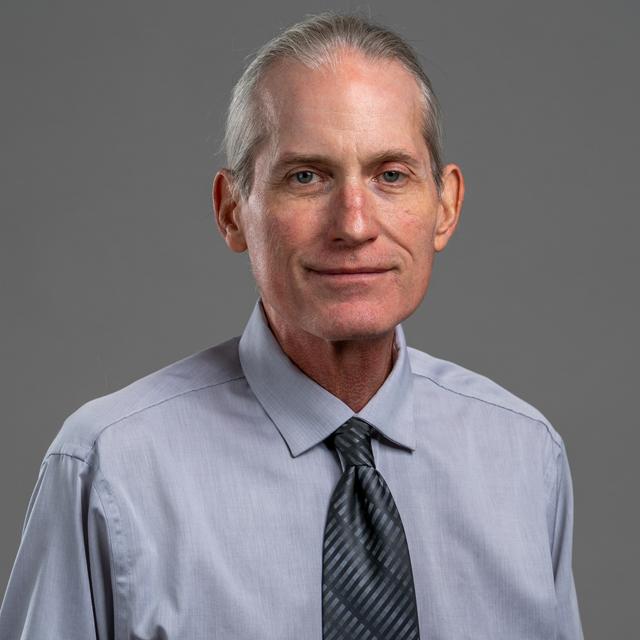 Tom Haas poses for a head shot in front of a gray background.