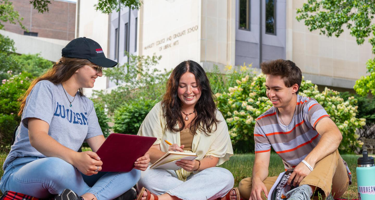 students sitting on the grass on campus, studying on laptops