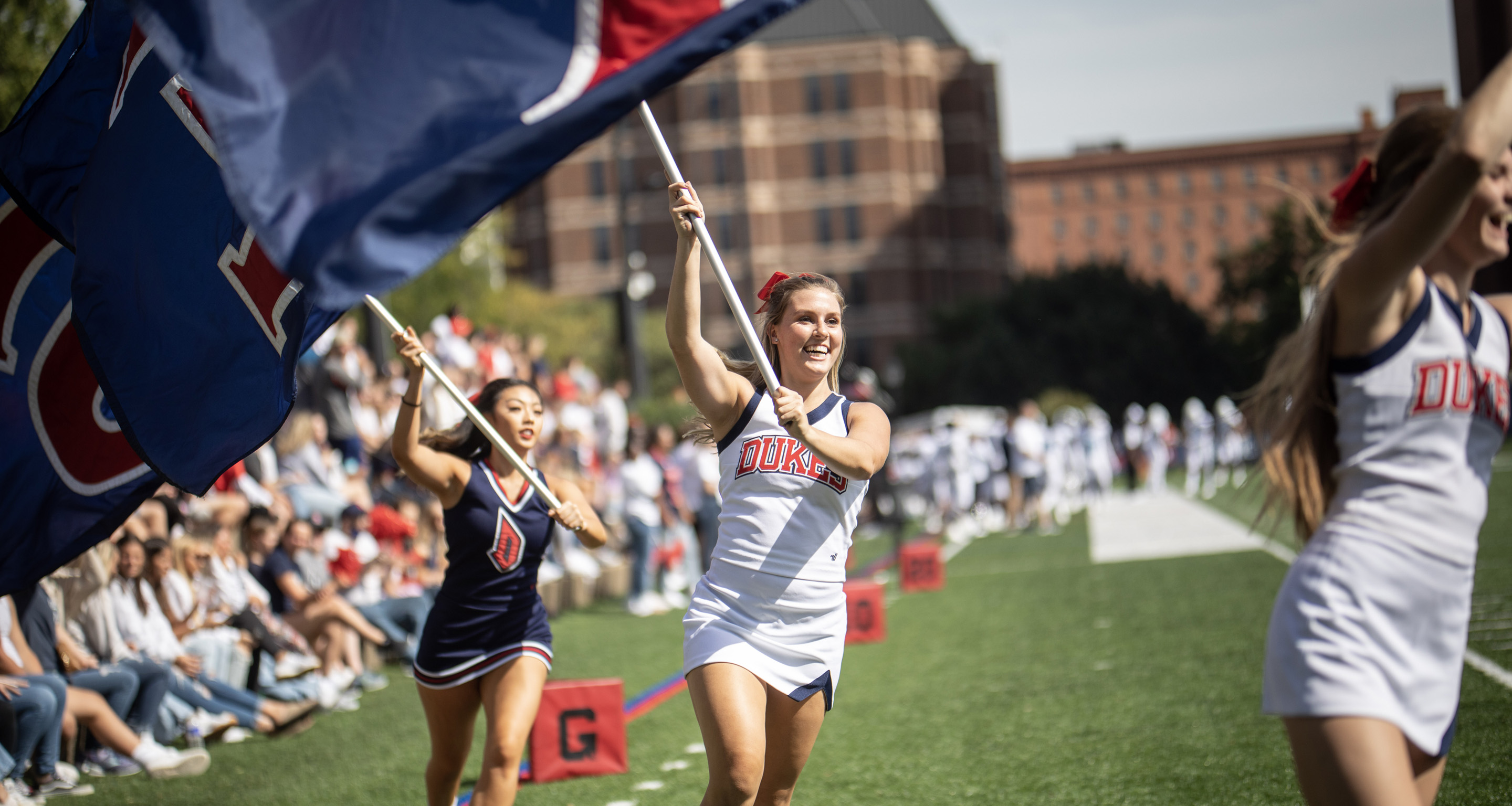 Duquesne Cheerleads running on Rooney Field with Duquesne banners.