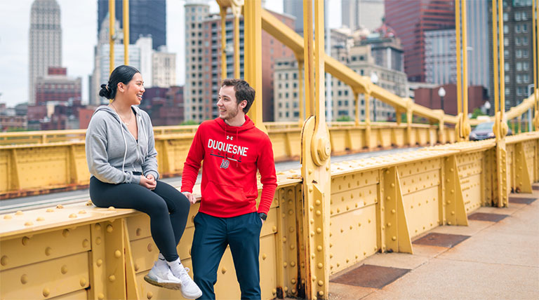 female and male student in Duquesne gear on Rachel Carson Bridge Pittsburgh