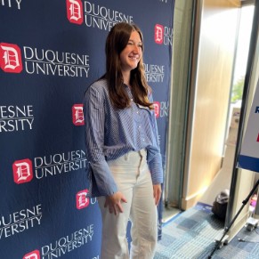 Young woman wearing professional clothing posing in front of Duquesne photo backdrop