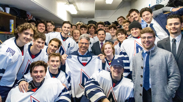 ice hockey team posing with President Ken Gormley in locker room