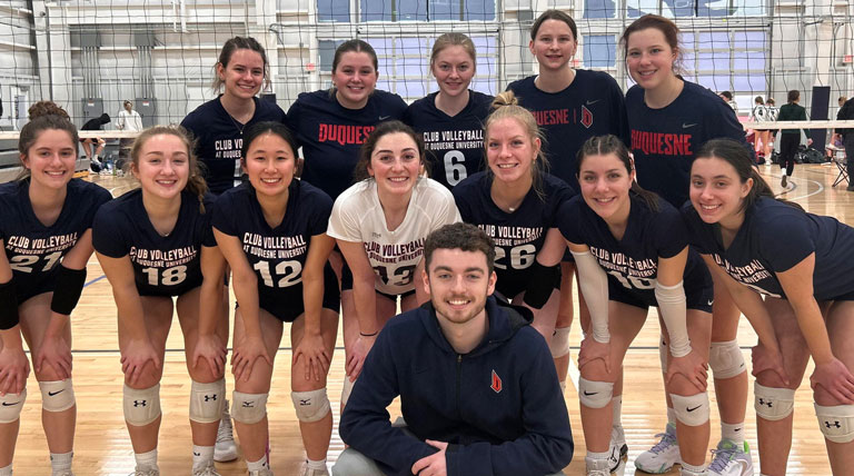 volleyball team posing together on court with volleyball net in background