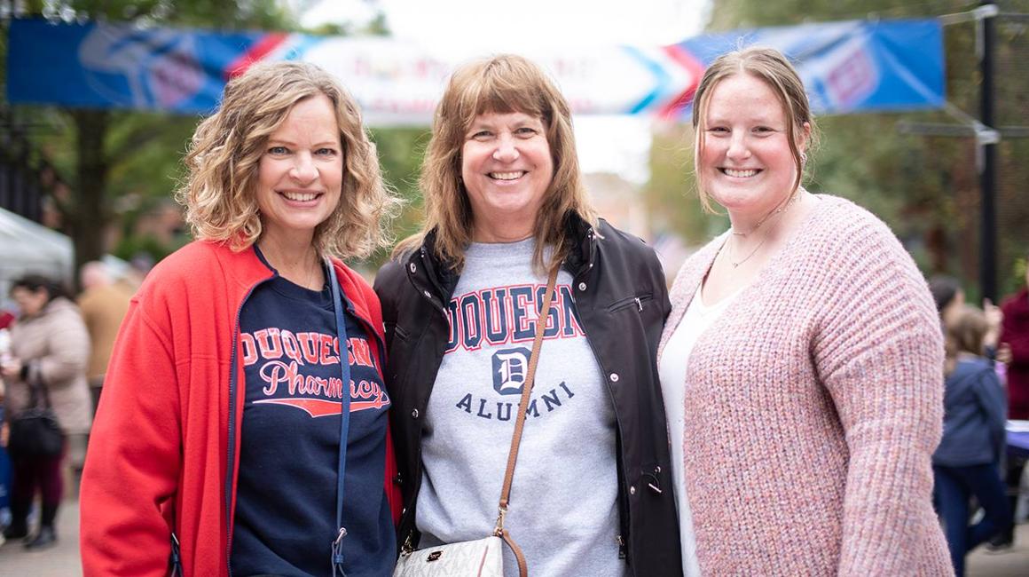 Family stands on Academic Walk smiling, wearing Duquesne attire