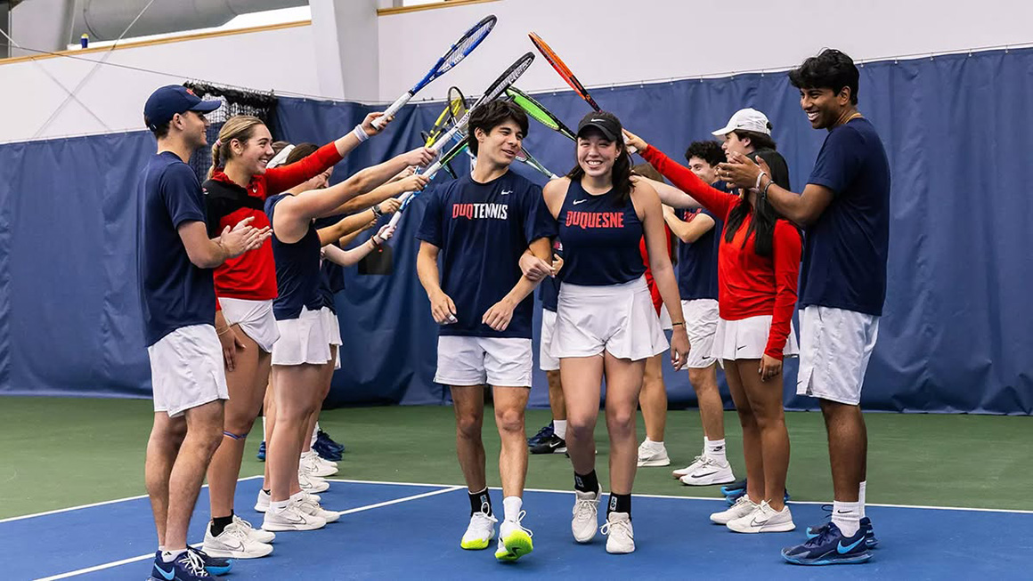 Duquesne club sports students walking through tennis rackets being raised by other club sports students