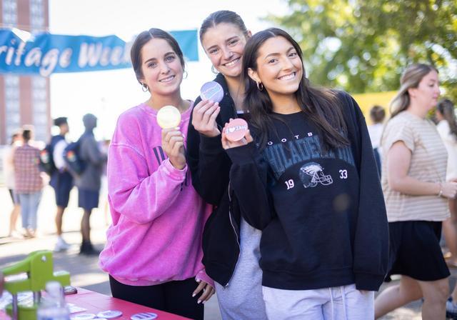 Three students pose, holding I (heart) DU buttons, during Heritage Week.