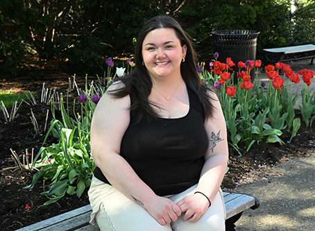 Cassidy Klock sits on a bench on Academic Walk with blooming tulips in the background