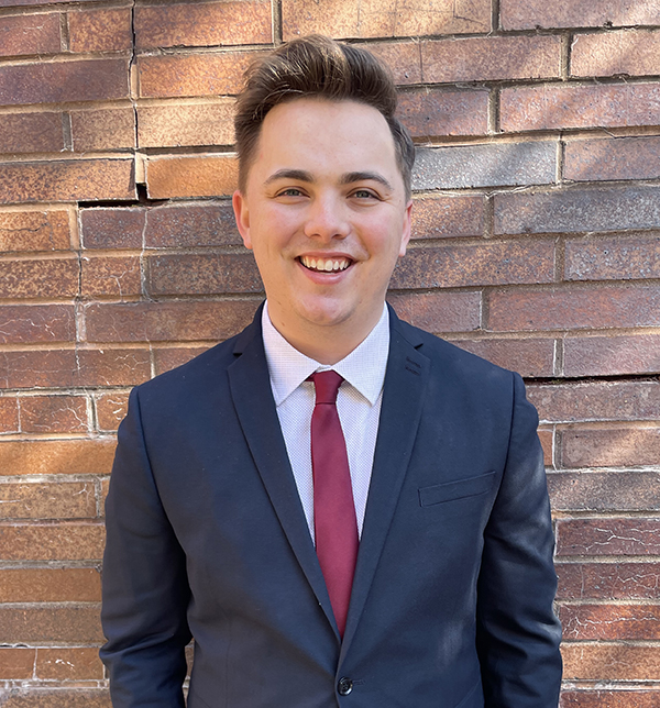 Daniel Smolsky in a suit standing in front of a brick wall