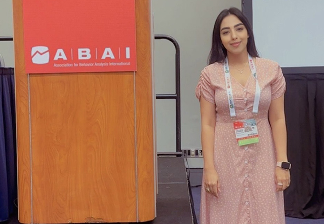 Duaa Alzahrani stands beside the podium at the ABAI conference.
