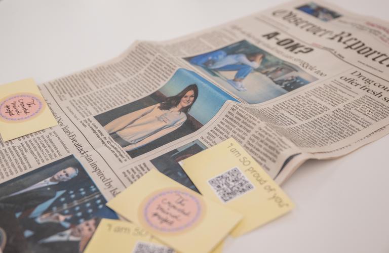 The front page of a newspaper is laid on a table with business cards placed on top.