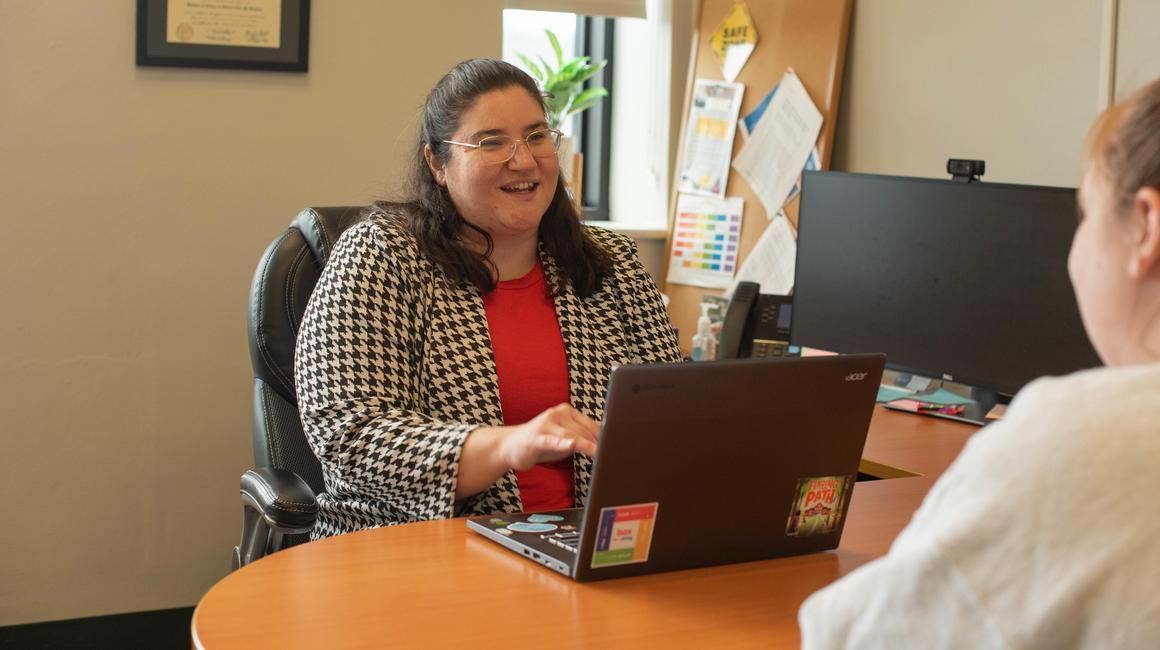 School psychology PhD student Athena Vafiadis sits at a desk and speaks with a School of Education student