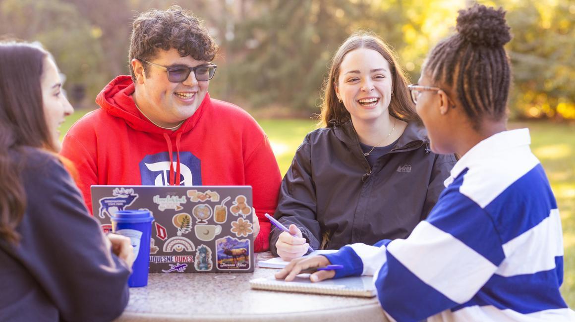Jack Maxwell sits at an outdoor table on campus with several friends