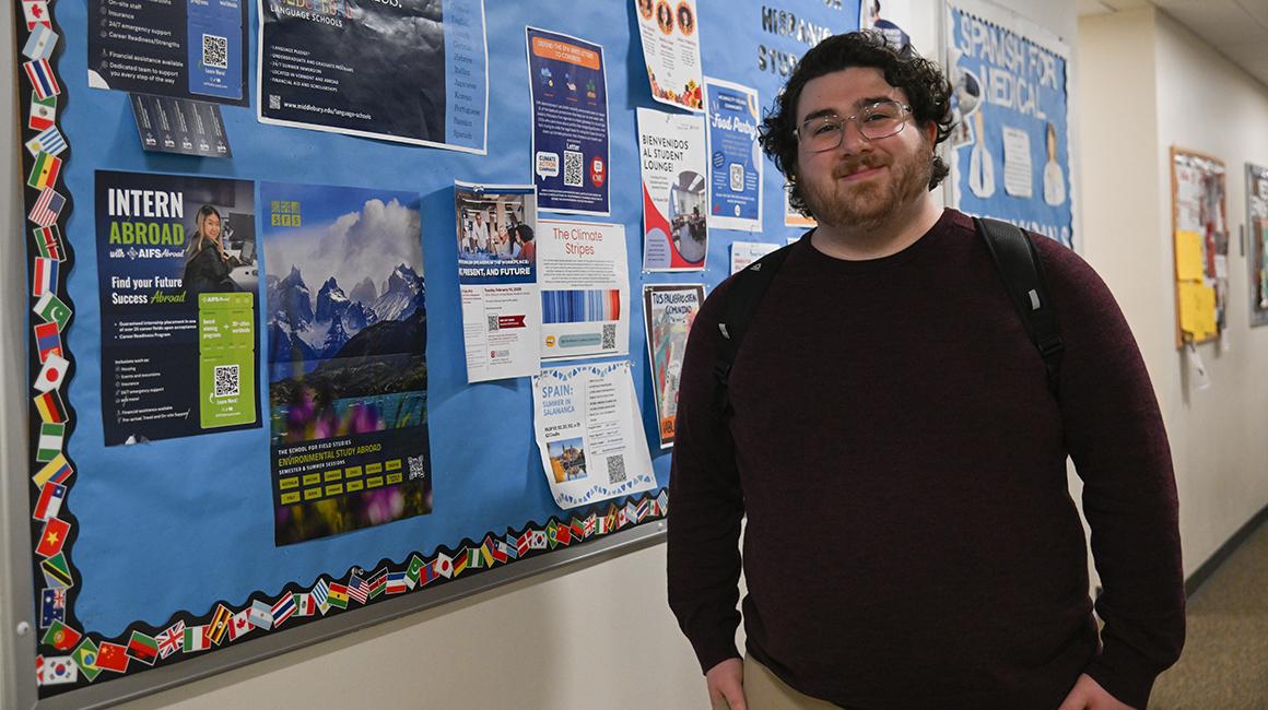 Nick Freilino stands outside the Center for Hispanic Studies against a bulletin board displaying opportunities within the Center