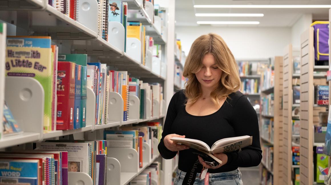 School of Education student Riley Adams looks at books in the Gumberg Library Curriculum Center
