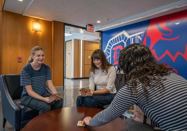Lexi plays cards with two friends at a table in the Gormley Student Union.