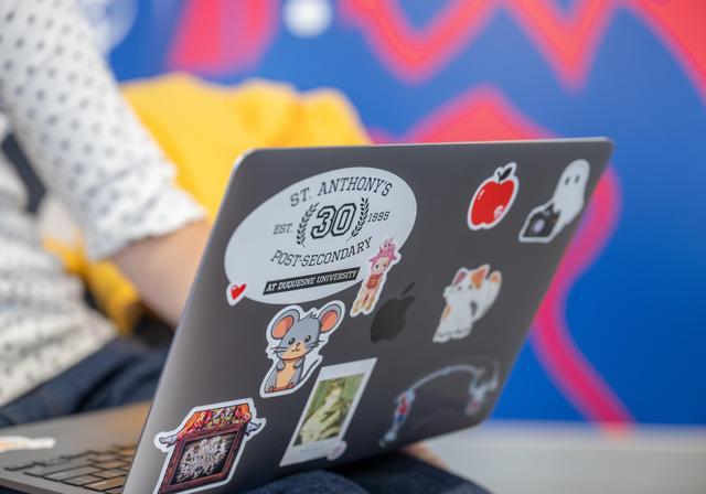 A laptop cover displays colorful stickers, including one that celebrates St. Anthony's post-secondary program at Duquesne