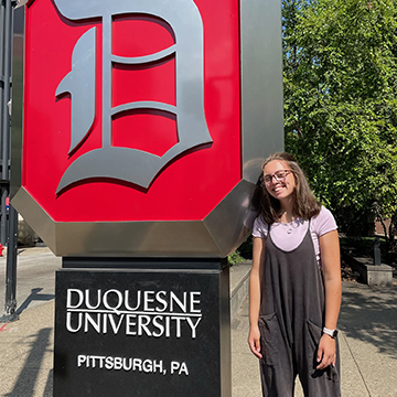 Maura Riscavage stands near the large Duquesne University sign on campus.
