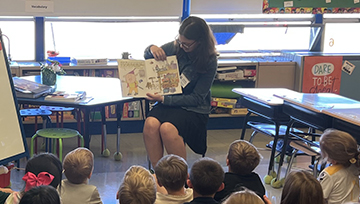 Maura Riscavage reads to students as they sit on the floor in front of her.