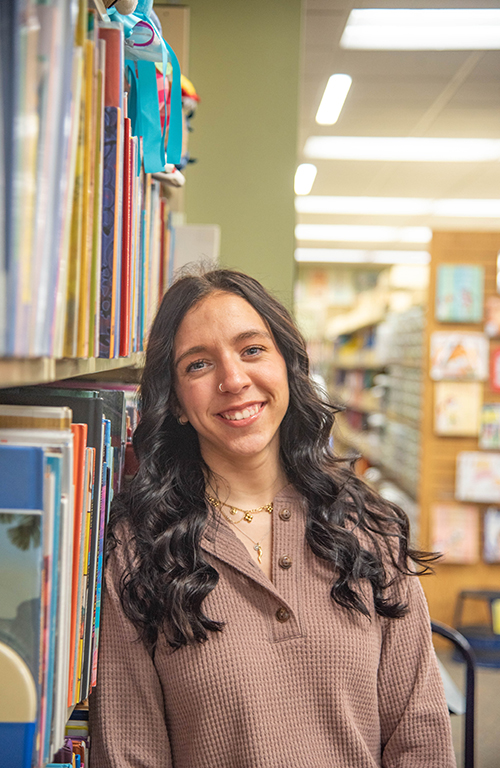 Headshot of School of Education student Caterina Veneziano in Curriculum Center standing in front of bookshelf