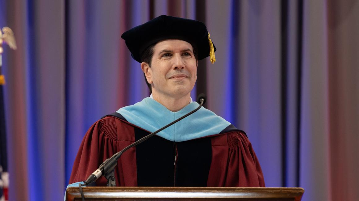 Dr. David Dausey at podium in graduation regalia