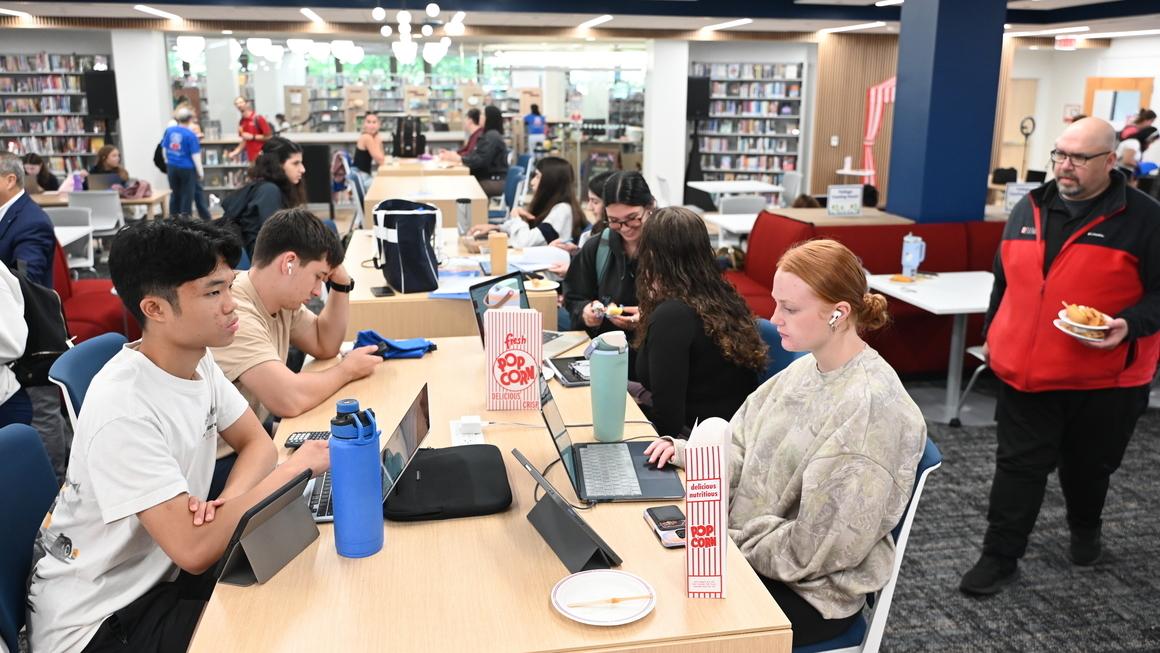 A group of students studies on laptops at a table.