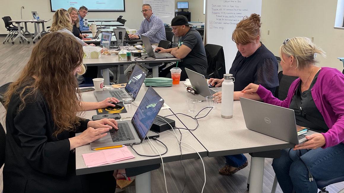 web editors and others working together at tables with laptops during the hackathon