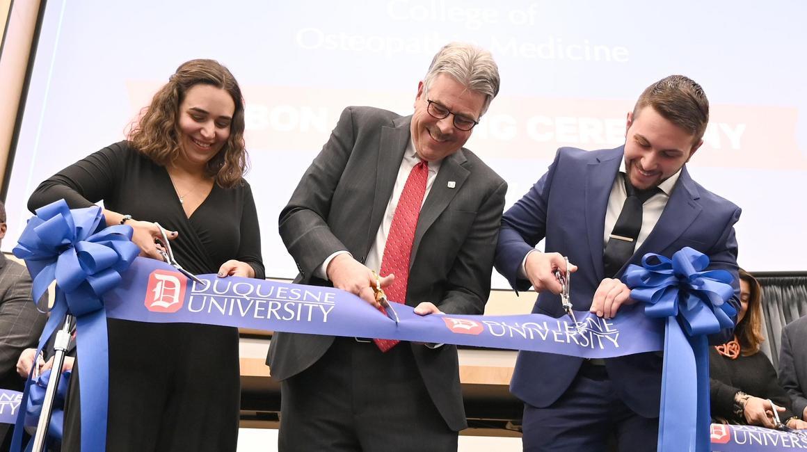 Ken Gormley and two med students cutting the ribbon for the opening of the COM.