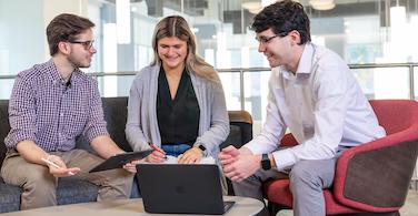 business school students smiling at one another while holding a laptop