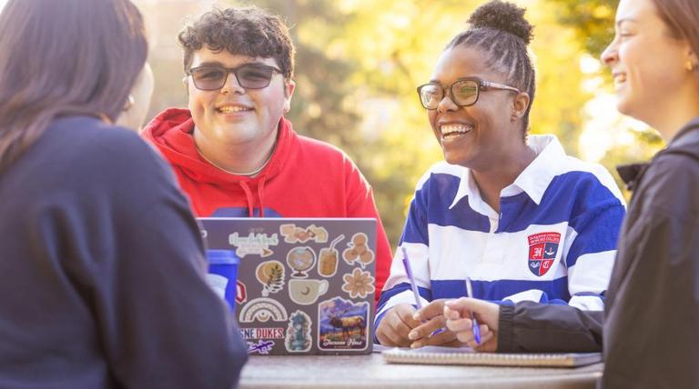 Student Jack Maxwell sits outdoors at a table and converses with classmates