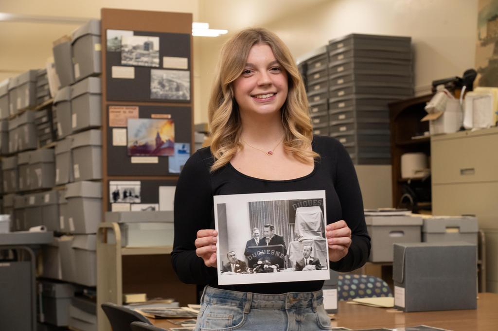 Riley Adams stands in DU archives holding a photo of her great-grandfather, Vernon Gallagher