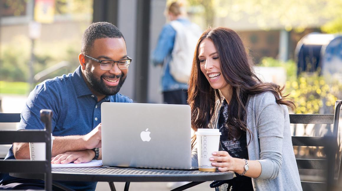 two students smiling while looking at computer screen