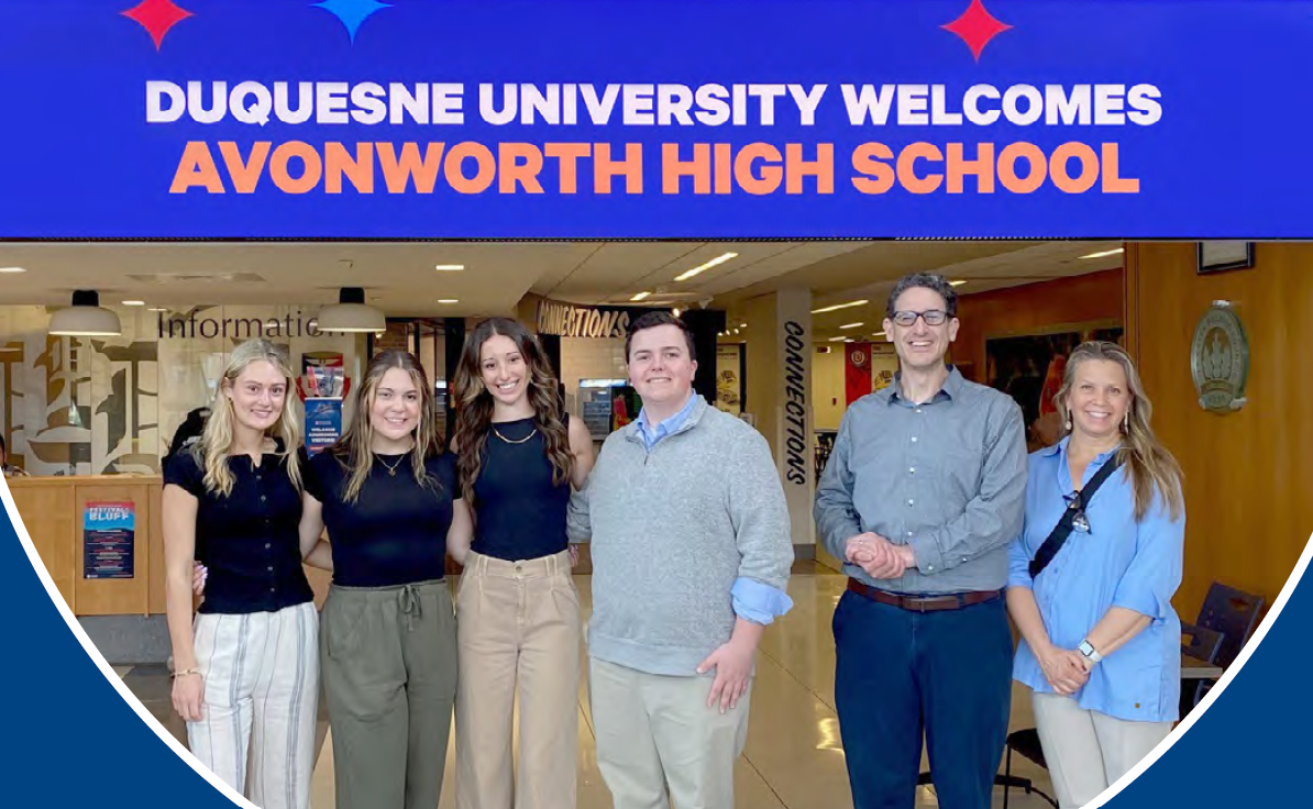 The four winners of the high school essay contest  and their teacher and district administrator stand under a banner that reads Duquesne University Welcomes Avonworth High School