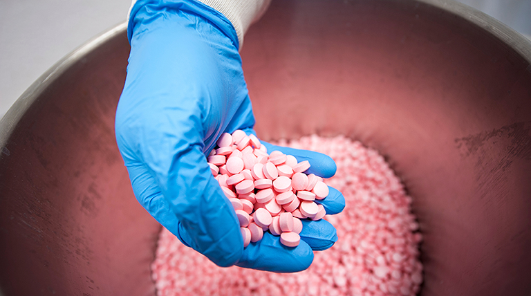 A gloved hand showing a handful of pink colored medicine.