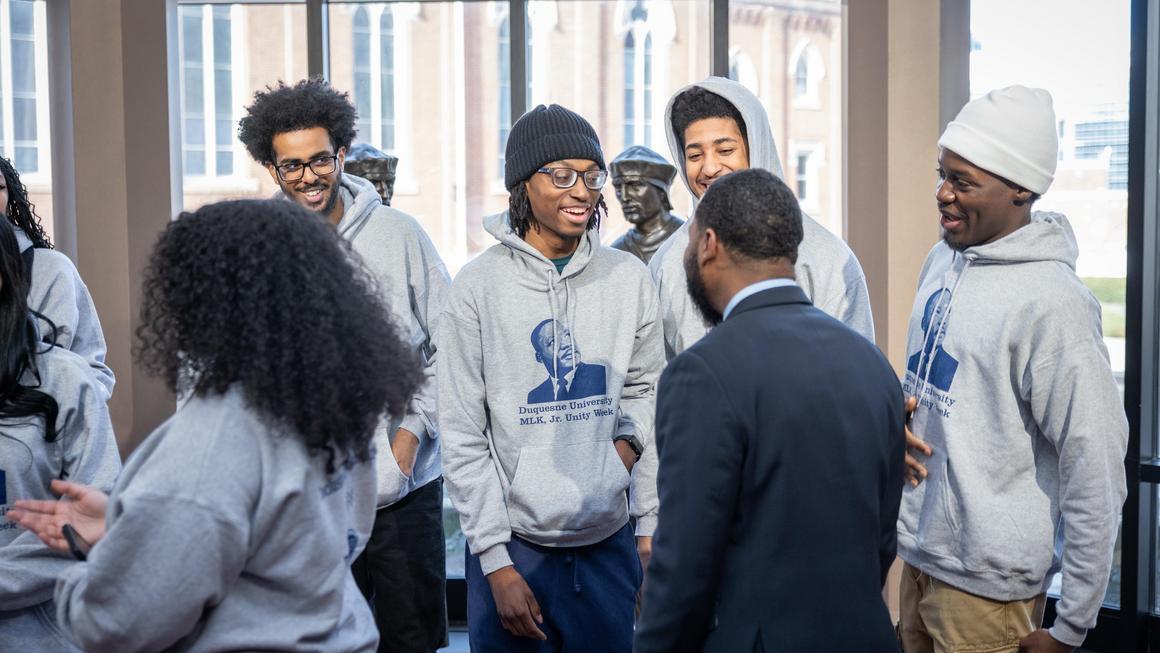 MLK Unity Walk 2026 students participants in gray MLK, Jr. hoodies talking with Quincy Stephenson in the Bayer Rotunda