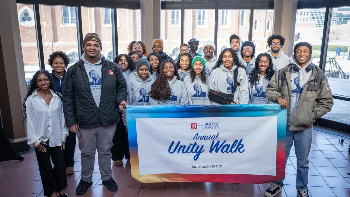 Group photo of student participants holding the Annual Unity Walk banner in the Bayer Rotunda at the MLK Unity Walk 2026 program