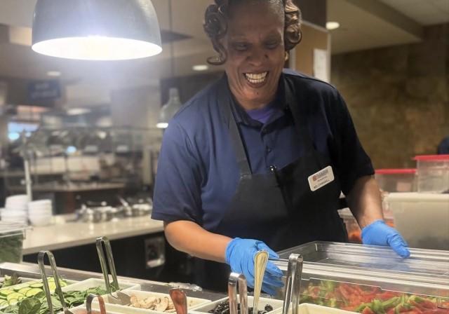A Towers food service worker smiles while serving salad bar.