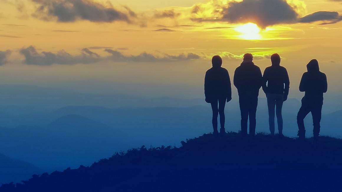 Four adults looking over a cliff at a blue horizon and yellow-gold sunset