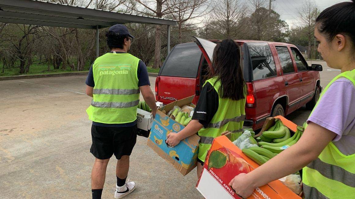 Students carry boxes of bananas to a car during a food drive.